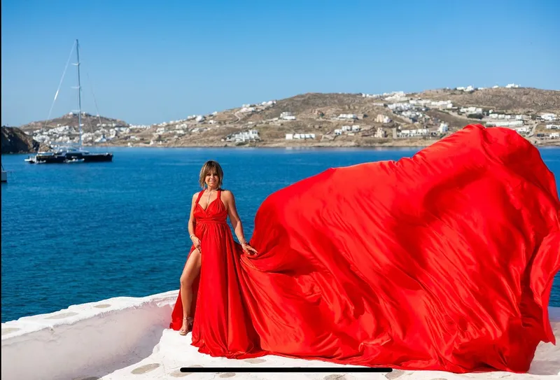 Woman in a red flying dress posing by whitewashed Paraportiani church on a Mykonos photoshoot